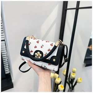 Close-up of white cherry print handbag with black woven handle and gold flower clasp