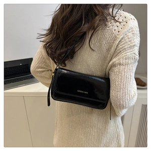 Detail of a shiny black patent leather shoulder bag with gold logo on a model