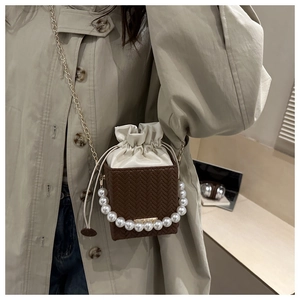 Brown woven crossbody bag with pearl handle and white drawstring on a model in trench coat