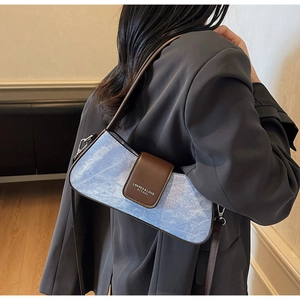 Detail of blue denim baguette bag with brown leather trim and metallic hardware accents