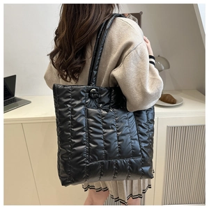 Detail of a black quilted puffer tote bag worn on shoulder in a cozy home office setting