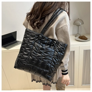 Close-up of black quilted puffer tote bag with silver hardware on warm studio background