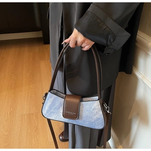 Detail of blue textured fabric bag with brown leather flap and silver metal hooks