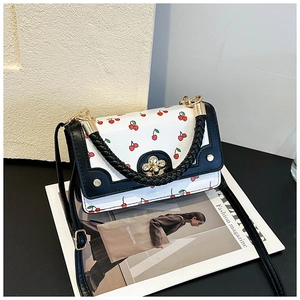 Close-up of white crossbody bag with cherry patterns and gold floral clasp detail