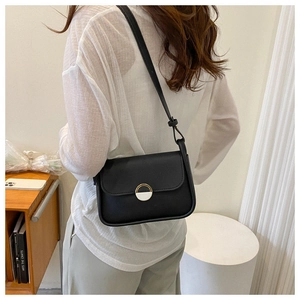 Detail of a black leather crossbody bag with a unique round decorative metal buckle