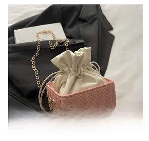 Close-up of pink woven bucket bag featuring pearl handle and gold chain strap detail