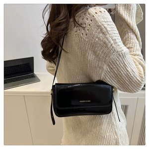 Detail of black patent leather shoulder bag with gold logo on white knit outfit
