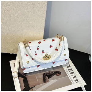 Detail of white cherry handbag featuring a floral gold lock and woven handle on magazines