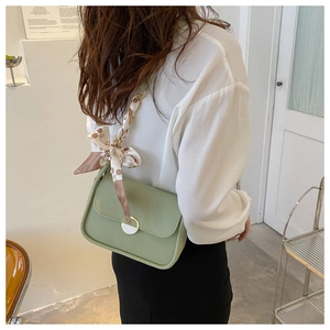 Detail of light green leather shoulder bag featuring a metal buckle and silk scarf strap