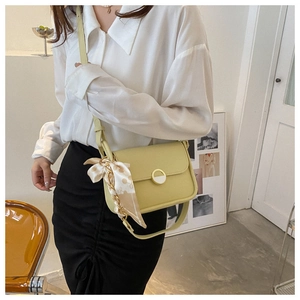 Detail of light yellow square bag with silk scarf on strap and round gold buckle