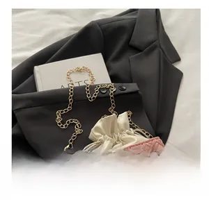 Detail of pink woven handbag with pearl handle and golden chain on a white surface