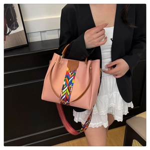 Pink faux leather tote bag with colorful woven strap details shown in lifestyle setting