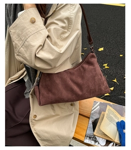 Close-up of brown suede shoulder bag with metal zipper worn by a model in autumn scenery