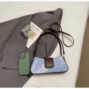 Detail of light blue denim baguette bag with brown leather trim and dual straps