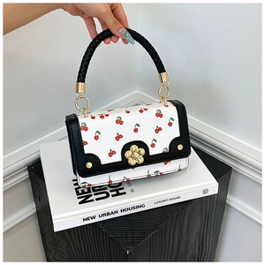 Detail of cherry print mini bag with braided handle and golden flower clasp closure