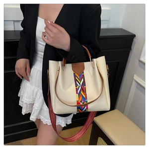 Close-up of cream tote bag with brown handles and colorful geometric embroidery strap