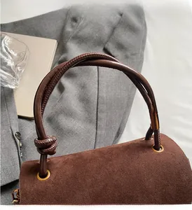 Close-up of brown suede handbag featuring intricate woven knot handle and brass eyelets