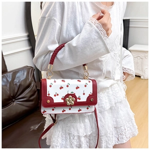 Detail of cherry print crossbody bag with gold flower clasp and woven handle