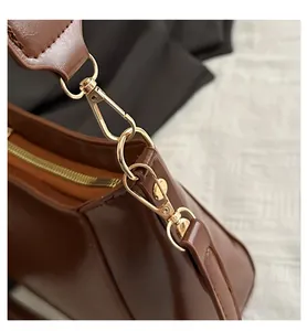 Macro shot of polished gold-tone metal hook and smooth brown leather bag strap detail