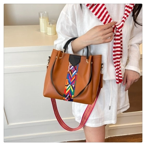 Brown tote bag with colorful woven stripes and a pink canvas shoulder strap in a lifestyle shot