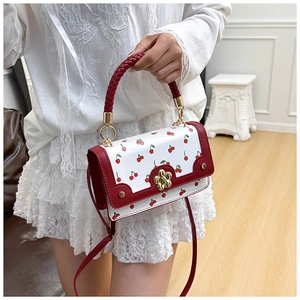 Close-up of woven handle detail and cherry print on white crossbody bag with floral lock