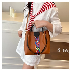 Close-up of brown faux leather handbag featuring colorful geometric woven strap detail