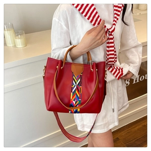 Detail of red leather tote bag featuring a colorful geometric strap and brown handles