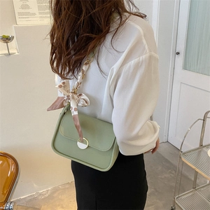 Light green underarm bag with silk scarf decoration and gold chain strap on model