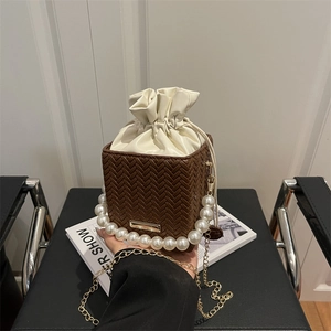 Brown woven box bag with pearl handle and drawstring closure shown in a lifestyle setting