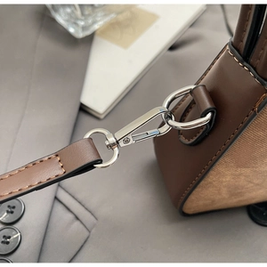 Close-up of silver metal lobster clasp and brown leather strap on a shoulder bag