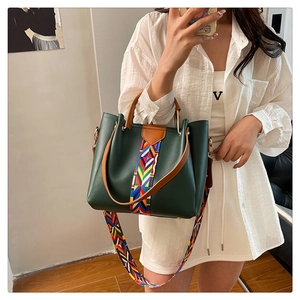Close-up of dark green leather handbag with colorful geometric woven straps and brown handle