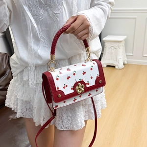 Chic white crossbody bag with cherry prints, red woven handle and gold sunflower clasp