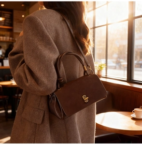 Brown faux suede square handbag with gold rotating lock shown in a cozy cafe setting