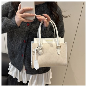 Détail d'un sac à main carré bicolore avec lettrage doré et finition en cuir lisse