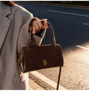 Brown faux suede crossbody bag with elegant gold geometric buckle on a city street