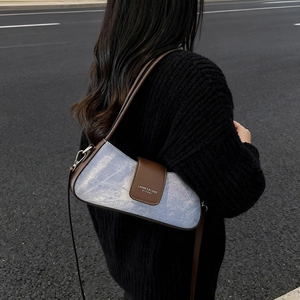 Denim underarm bag with leather trim and magnetic flap shown in an outdoor street setting
