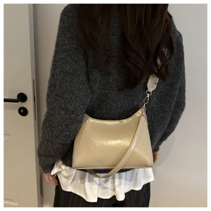 Detailed back view of a beige glossy patent leather baguette shoulder bag on model