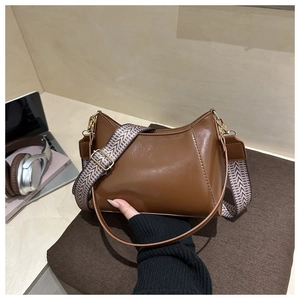 Detail of brown faux leather half-moon bag featuring wide chevron woven shoulder strap