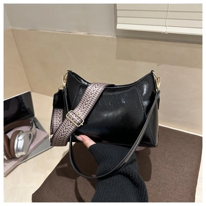 Detail of black semi-moon underarm bag with decorative woven strap and gold-tone hardware