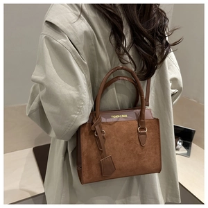Détail du sac à main marron en daim avec logo doré porté par un mannequin en intérieur