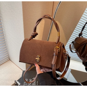 Detail of dark brown suede handbag featuring unique knotted handle and gold turn-lock closure