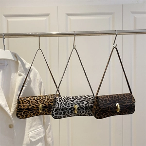 Three leopard print baguette shoulder bags with gold metal clasps hanging on a wall
