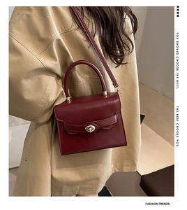 Detail of burgundy leather handbag with gold metal lock worn over a beige trench coat