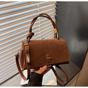 Detail of suede textured flap and gold twist lock on dark brown crossbody bag