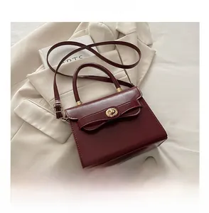 Borsa bordeaux con fiocco e chiusura dorata mostrata accanto a uno smartphone