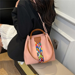 Pink faux leather tote bag with rainbow strap worn by a model in a minimalist setting