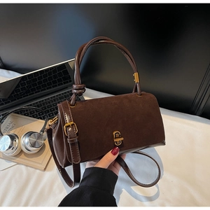 Close-up of suede crossbody bag with gold twist lock on a desk with a laptop