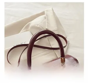 Dettaglio della borsa in pelle lucida bordeaux con manico semicircolare e hardware dorato