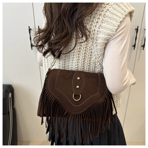 Dettaglio di una borsa a sella in pelle scamosciata marrone scuro con nappe su modella