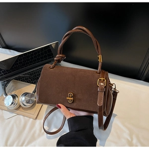 Detailed view of brown suede handbag featuring braided handle and golden twist lock